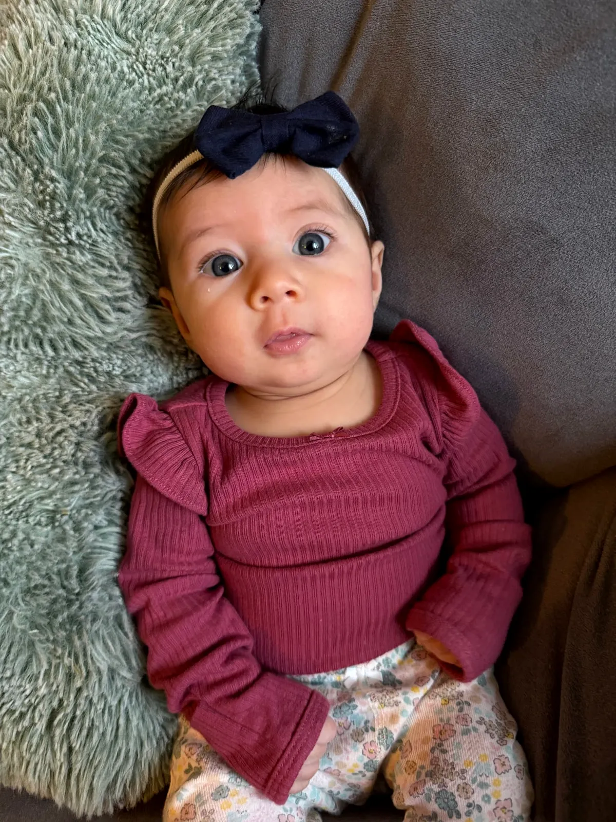 A young baby with a navy bow lying awake on a cozy couch