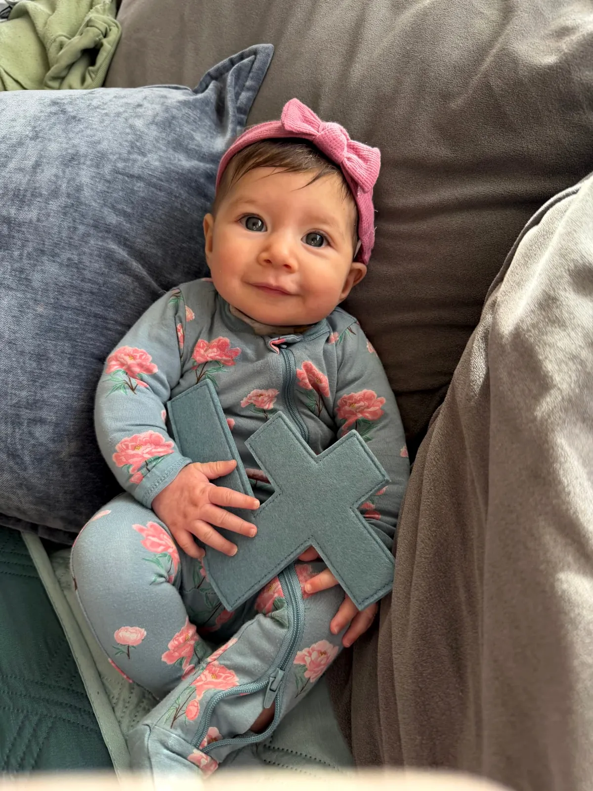A smiling baby in floral pajamas holding a felt letter